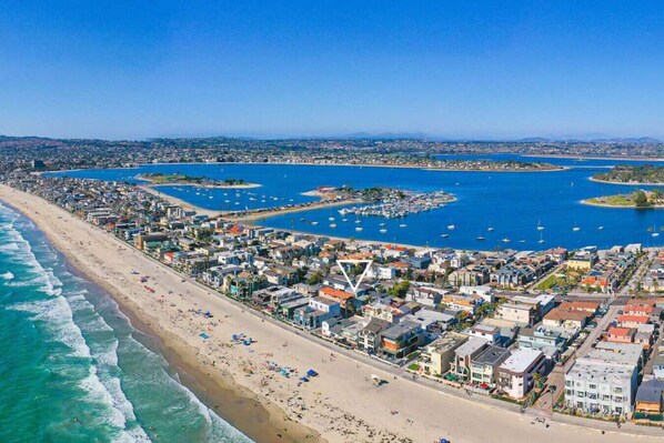 An aerial view of a coastal town with a beach, marina, and dense residential area.