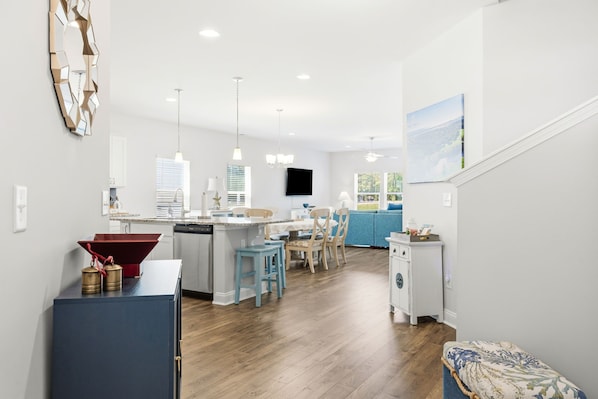 A modern kitchen with a central island, a dining area with blue chairs, and a living room with a blue sofa.