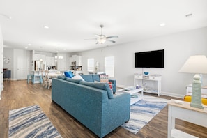 A modern living room with a blue sofa, a flat-screen TV, and a ceiling fan.