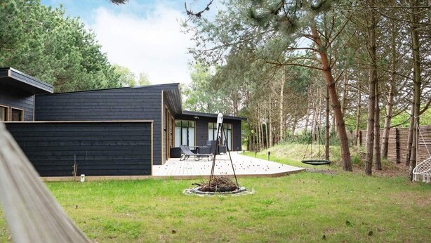 A modern house with a dark exterior, a covered patio with outdoor furniture, and a hammock in the foreground. - 5 Star Holiday Home in Sjaellands Odde (Sjællands Odde)
