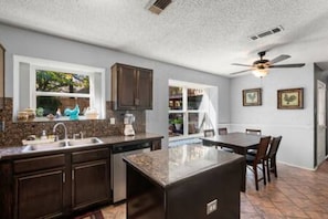 A kitchen with dark cabinetry, a granite countertop, a built-in island, and a ceiling fan. - Epic Stay Pool + Fire Pit + *Location* (Fort Worth)