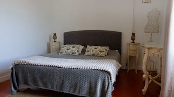 Un lit bien fait, avec une tête de lit grise, deux oreillers assortis, une couverture blanche et grise, et un petit ananas décoratif posé sur la table de chevet.