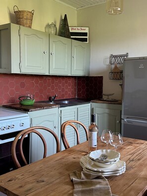 A kitchen with light green cabinets, a red hexagonal backsplash, a wooden table with plates and glasses, and a bottle of wine.