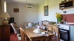 A dining area with a wooden table, chairs, a vase with flowers, and a kitchen area with a stove and cabinets. - Country house with a pool, 3 minutes from Vaison-la-Romaine. (VAISON LA ROMAINE)