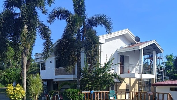 Un edificio de dos plantas con piscina, rodeado de palmeras y otra vegetación.