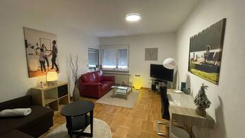 Ein modernes Wohnzimmer mit einem roten Sofa, einem runden schwarzen Tisch und einem Fernseher auf einem Schrank.