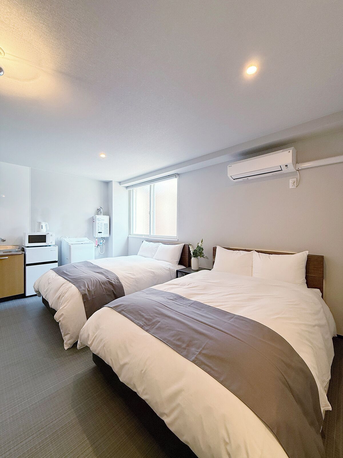 Hotellihuone, jossa on kaksi sänkyä, mikroaaltouuni, pieni keittonurkkaus ja ilmastointilaite.