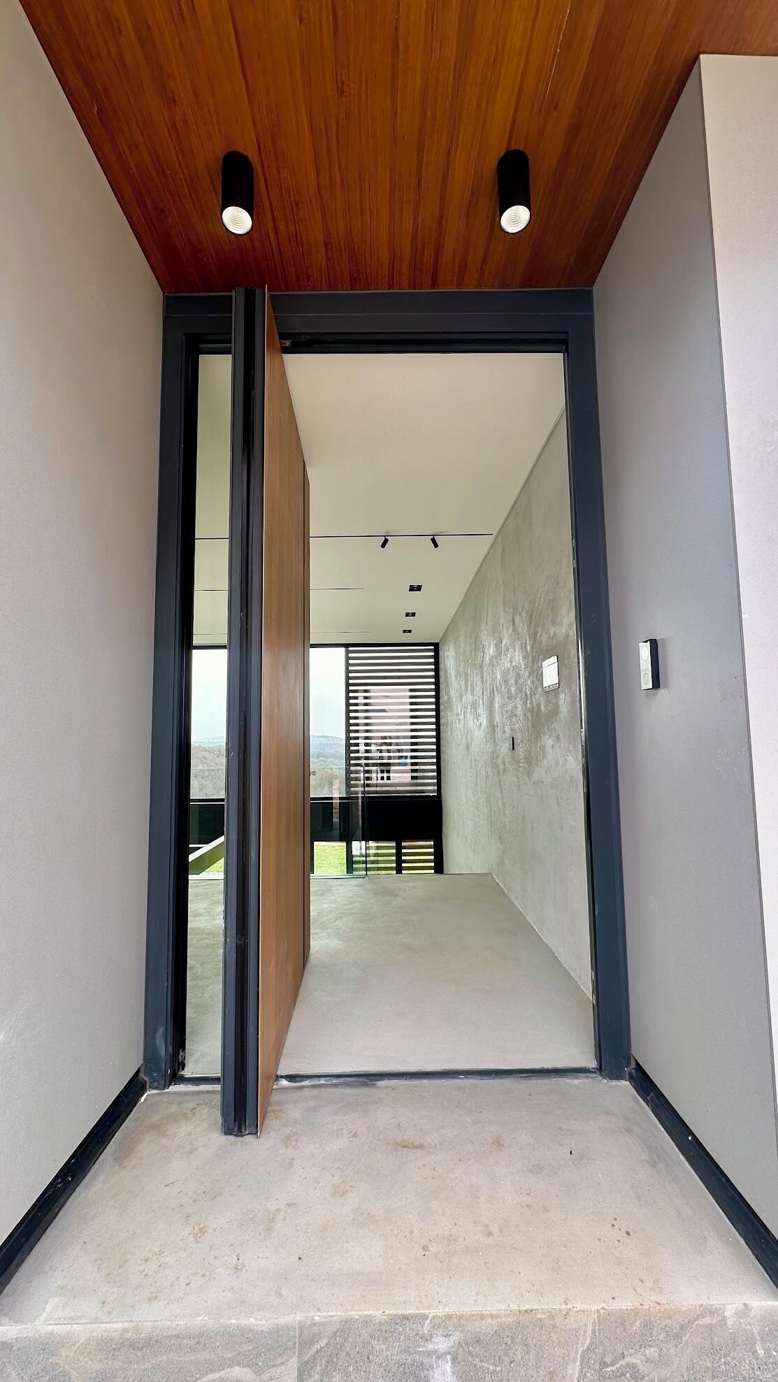 A modern interior with a wooden ceiling, a concrete floor, and a view of a balcony with a metal railing.