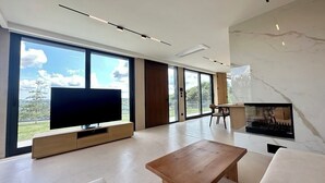 A spacious living room with a large TV, a fireplace, and large windows offering a view of the outdoors. - Beykoz Breeze (Beykoz)