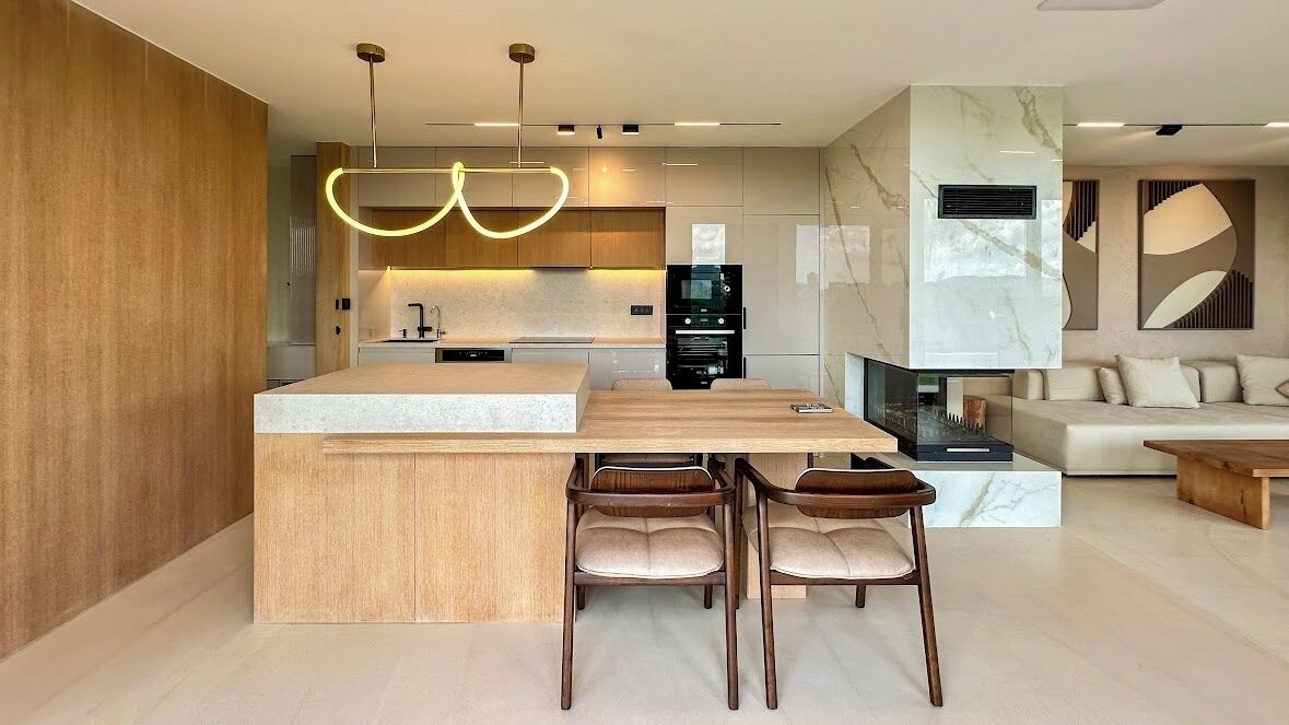 A modern kitchen with a central island, wooden chairs, and pendant lighting.