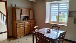 Un comedor con mesa y sillas de madera, un armario con cajones y una ventana con persianas.