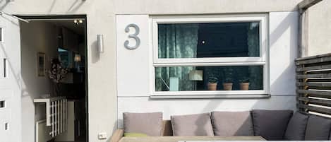 A modern exterior with a number '3' sign, a wooden bench, and a wicker sofa.