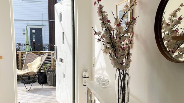 A room with a white door leading to an outdoor area with a chair and a table. There is a vase with flowers on the table and a mirror on the wall. - 4 Star Holiday Home in Laholm (Skummesloevsstrand)