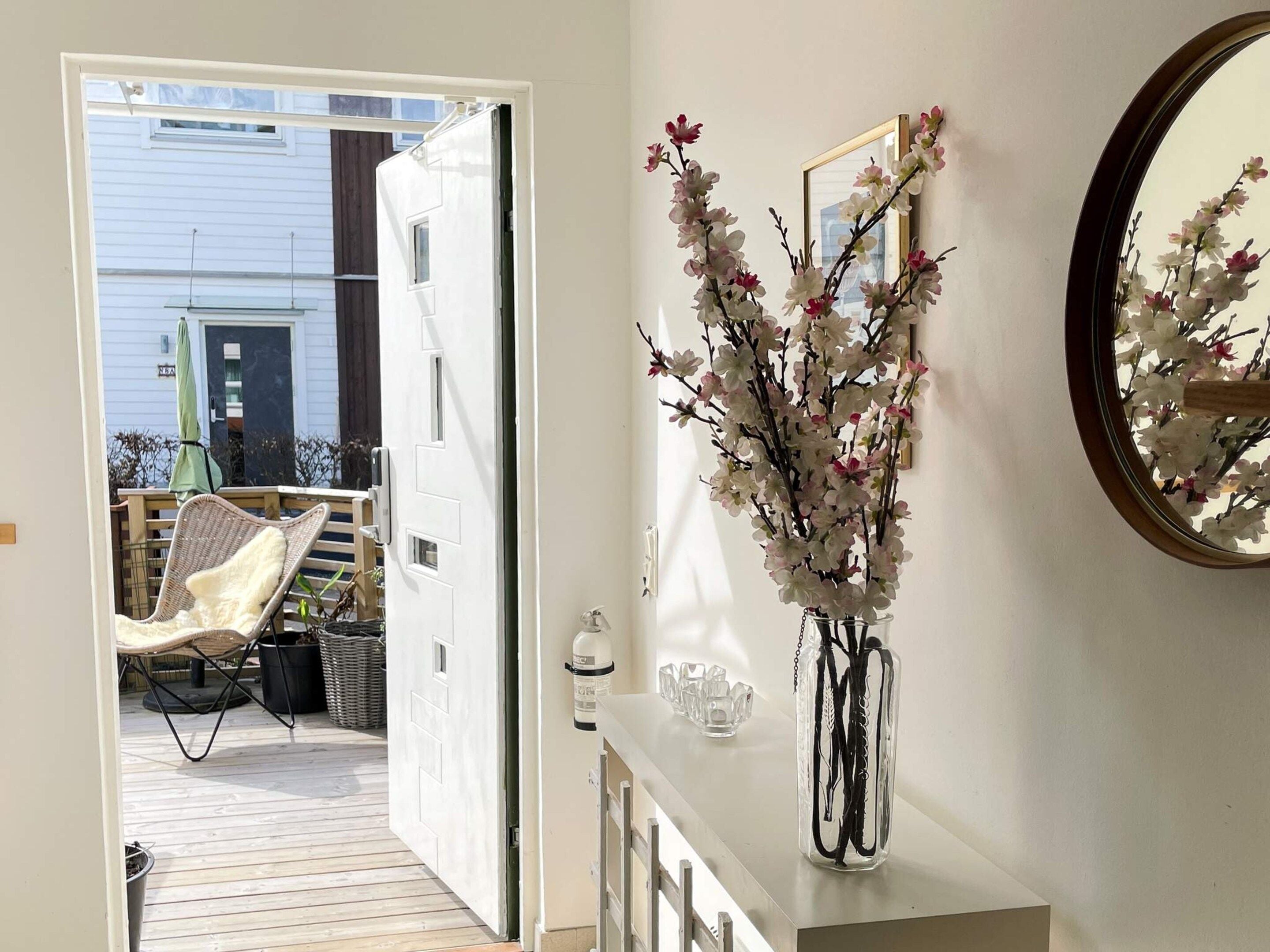 An open door leading to a deck with a chair and a table with a vase of flowers.