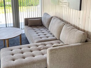 A sectional sofa with a tufted design, a round coffee table, and a large flat-screen TV mounted on a wooden wall.