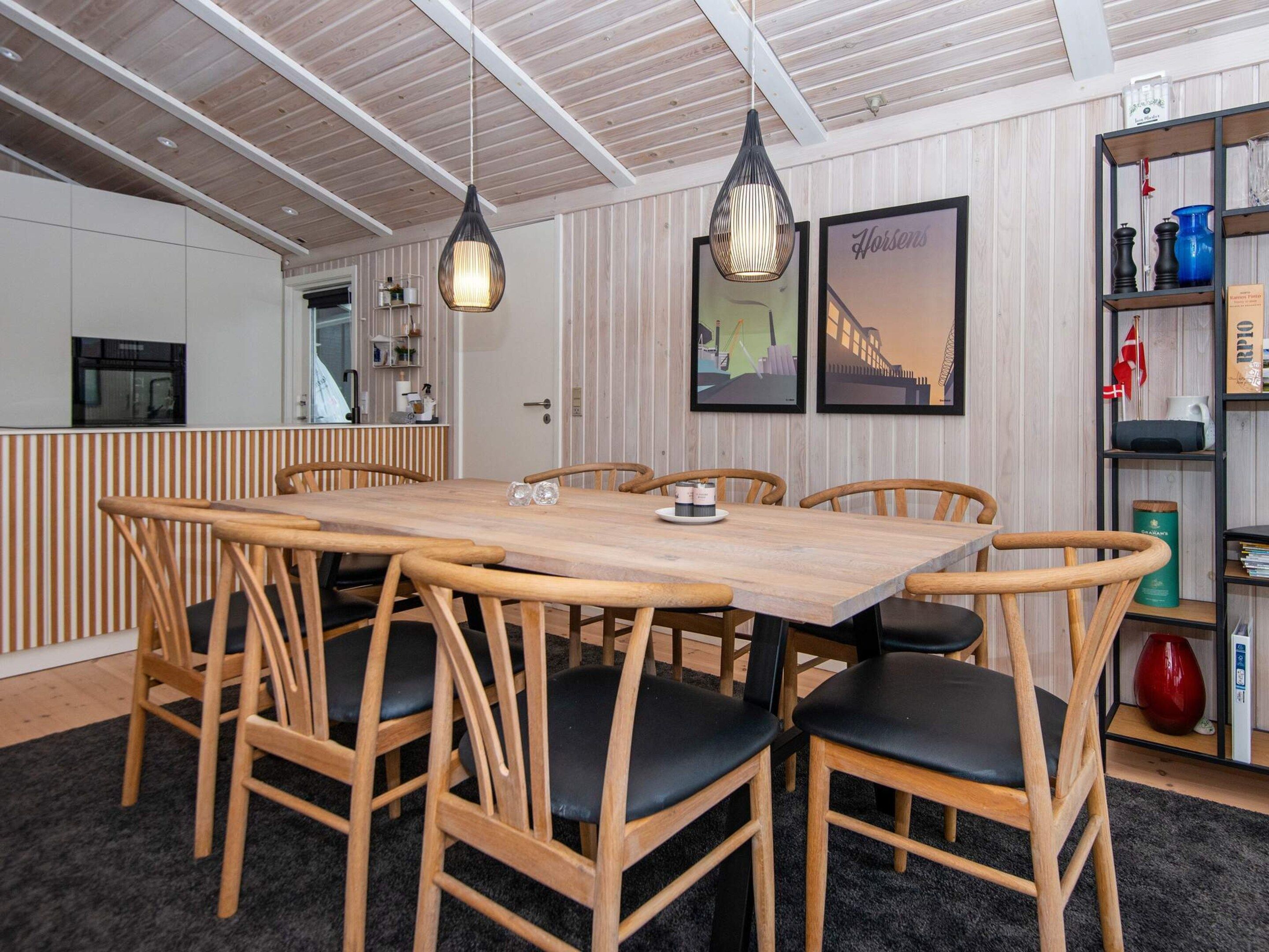A dining area with a wooden table and chairs, pendant lights, and framed artwork on the wall.