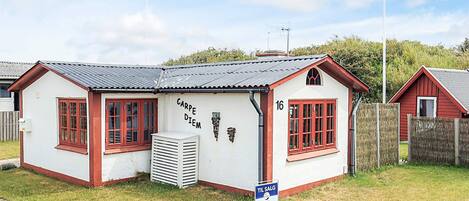 A small building with a white exterior and red trim, featuring a number '16' on the side, a sign reading 'TIL SALG,' and a small air conditioning unit in front.
