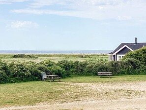 A house with a dark roof and white trim, surrounded by a grassy field and dense shrubbery. - 6 Person Holiday Home in Logstor (Logstor)