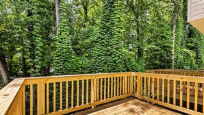 A wooden deck with a railing, surrounded by dense green foliage.