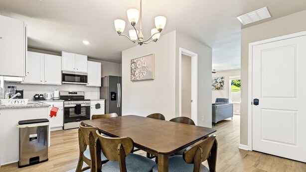A modern kitchen with white cabinets, a wooden dining table, and a chandelier.