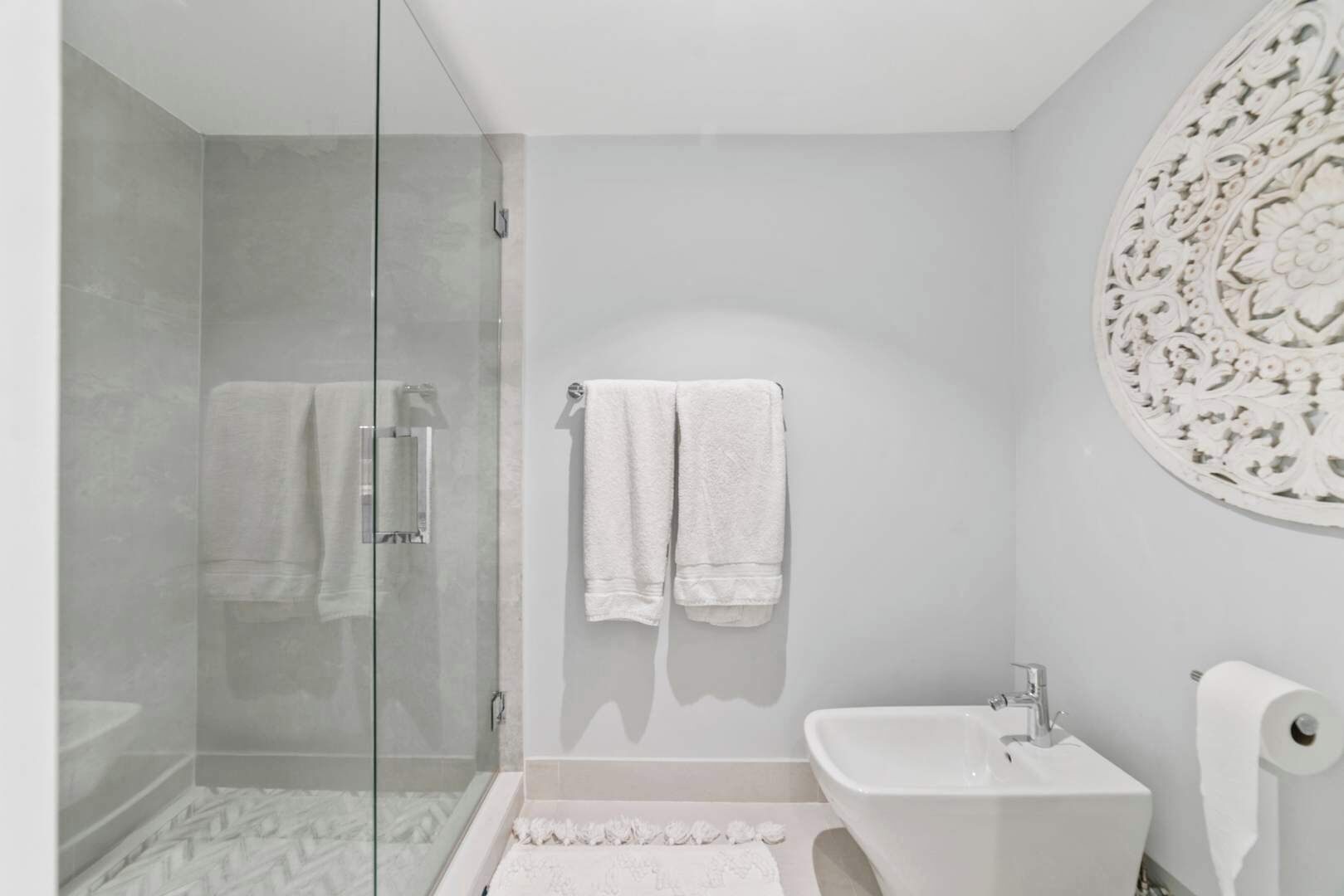 Ein modernes Badezimmer mit Duschkabine aus Glas, einem weißen Waschbecken und einem dekorativen Wandelement.