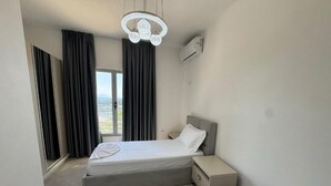 A hotel room with two beds, a large window with curtains, an air conditioning unit, and a modern chandelier. - Rana E Hedhun Apartment (Lezha)