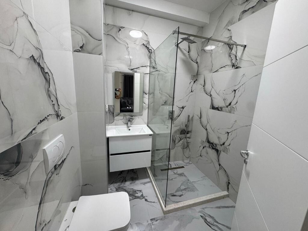 A modern bathroom with a glass shower enclosure, a white sink, and marble-patterned walls.