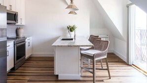 A modern kitchen with white cabinetry, a built-in microwave, a stainless steel oven, and a wooden floor. - Historic City View Loft - Walk to Newport's Best (Newport)