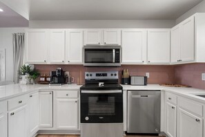 Eine moderne Küche mit weißen Schränken, einer Edelstahl-Mikrowelle, einem Backofen und einem Geschirrspüler.