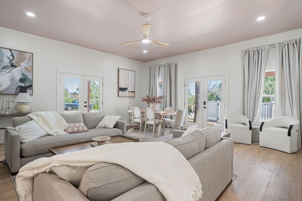 A spacious living room with a sofa, chairs, a dining table, and a ceiling fan.