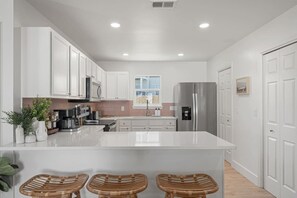 A modern kitchen with white cabinets, a stainless steel refrigerator, and a central island with bar stools.