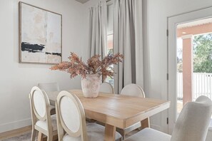 Ein Essbereich mit einem Holztisch, vier Stühlen, einer Vase mit Trockenpflanzen und einem Bild an der Wand.