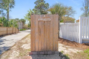 A wooden gate with a sign reading 'EASY STREET' in a residential area with a paved driveway, a white fence, and trees.
