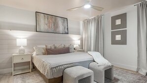 Ein Schlafzimmer mit einem Bett, Nachttischen, einem Deckenventilator und einem großen abstrakten Gemälde.