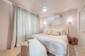 A bedroom with a bed, curtains, a ceiling fan, a wall-mounted light, and a rug.