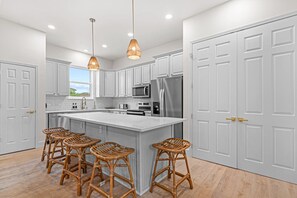 A modern kitchen with white cabinetry, a large island with bar stools, stainless steel appliances, and pendant lighting. - 4BDR~Renovated Home with Private Pool (Destin)