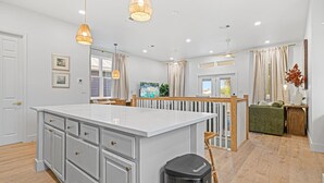 Una cocina amplia con una isla grande, luces colgantes y vista al comedor.