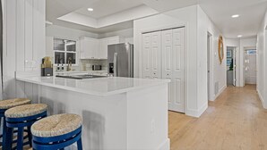 A modern kitchen with white cabinetry, a central island, and a bar area with stools. - 5BDR Renovated Home~Private Pool + Games (Destin)