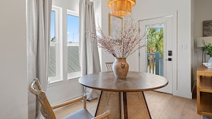 A dining area with a round table, wicker chairs, a vase with branches, and a wooden ceiling light fixture. - 5BDR Renovated Home~Private Pool + Games (Destin)