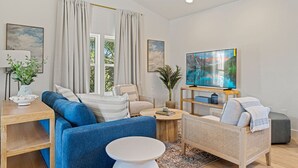 A modern living room with a sofa, armchair, coffee table, and a TV on a stand. - 5BDR Renovated Home~Private Pool + Games (Destin)