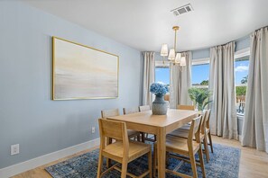 Un coin repas avec une table et des chaises en bois, un vase rempli de fleurs, un tableau accroché au mur et une vue par la fenêtre.