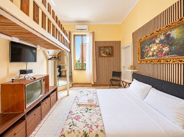 A hotel room with a bed, a television, a desk with a computer, a chair, and a painting on the wall.