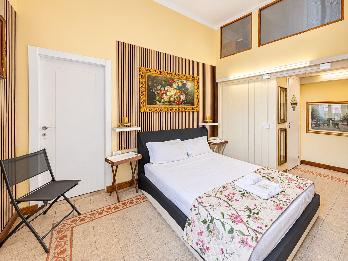 A hotel room with a bed, a chair, a painting on the wall, and a door.