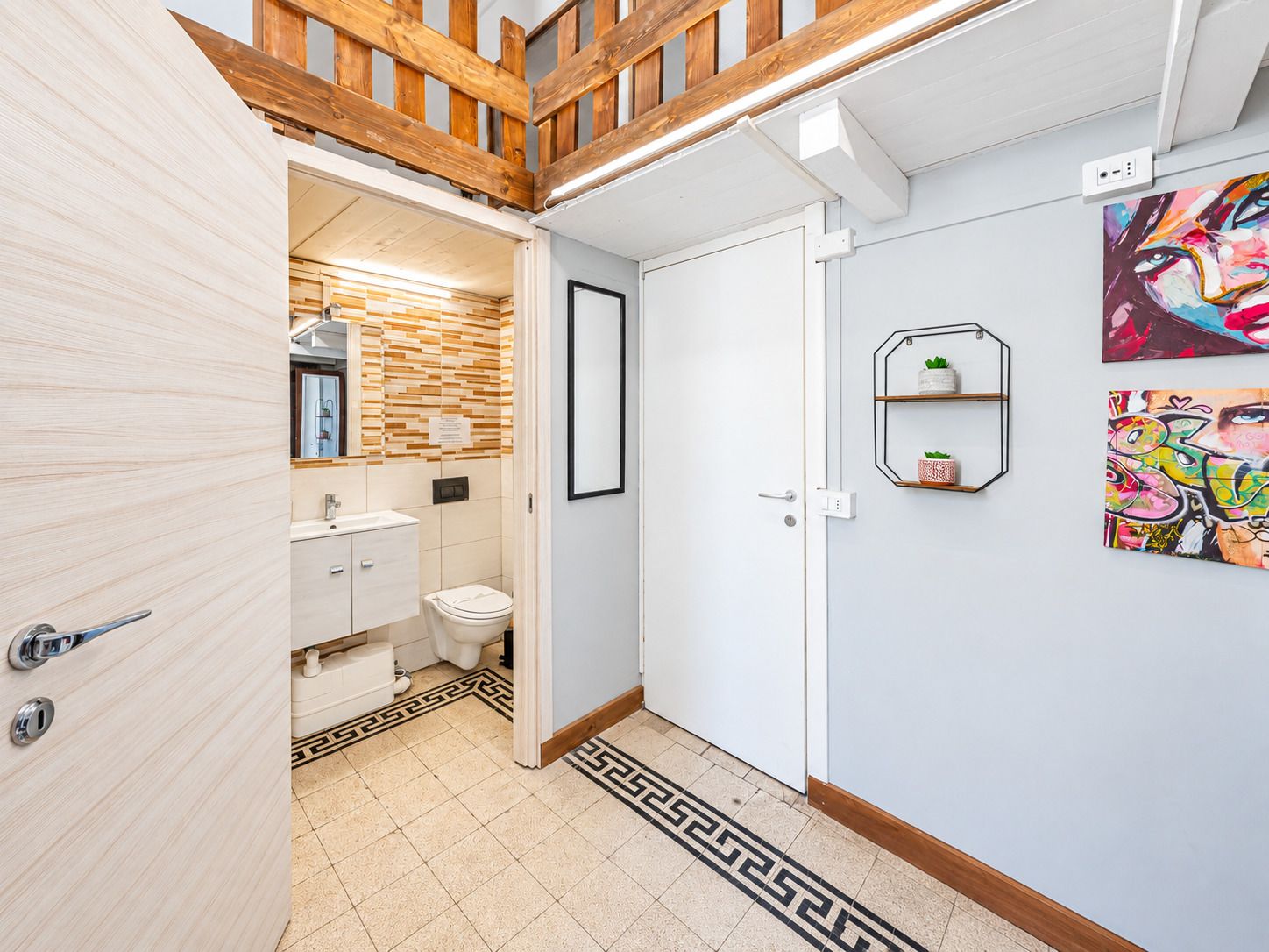 A modern bathroom with a wooden ceiling, a white sink, and a toilet. There are two framed artworks on the wall.