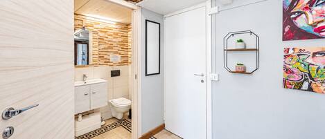A modern bathroom with a wooden ceiling, a white sink, and a toilet. There are two framed artworks on the wall.