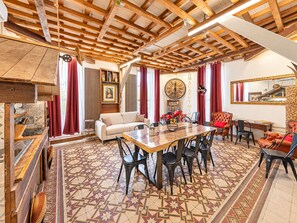 Un'ampia zona giorno con soffitto alto, un tavolo da pranzo con sedie, un divano e un orologio grande appeso al muro.
