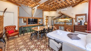 A cozy room with a wooden ceiling, a dining area with chairs, a bed with pillows, and a TV mounted on the wall.