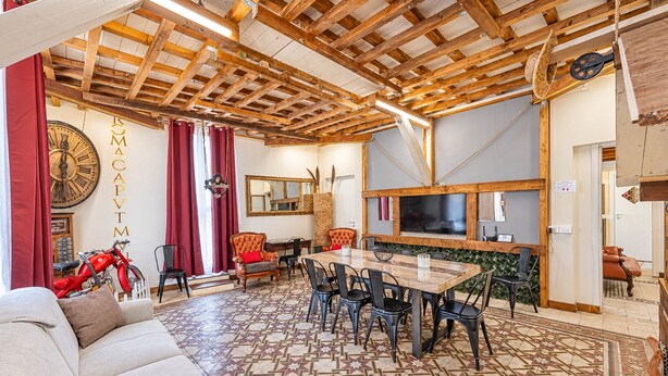 A spacious living area with a wooden ceiling, a large clock, a dining table with chairs, and a sofa.