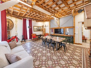 Un'ampia zona giorno con soffitto in legno, un orologio grande, un tavolo da pranzo con sedie e un divano.
