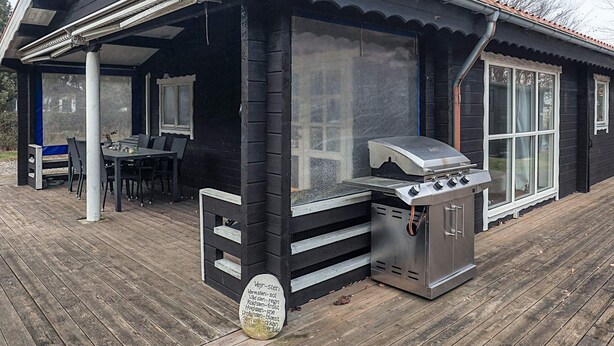 A covered outdoor area with a grill, a table with chairs, and a view of the surrounding area.